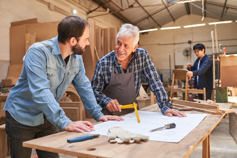 Artiste principal et apprenti charpentier avec un plan d'ensemble discutez d'un projet de construction de maison