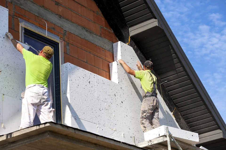 Deux ouvriers en gilets jaunes haute visibilité installent des panneaux d'isolation thermique extérieure sur façade de maison individuelle