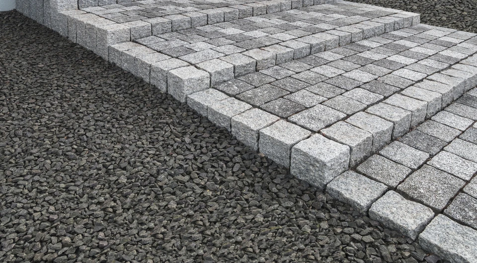 Chantier extérieur de pose de pavés en granit gris sur lit de graviers