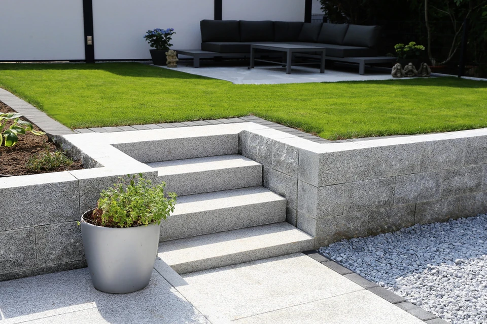 Aménagement paysager moderne avec escalier en blocs de béton gris et margelles blanches menant à une pelouse parfaitement entretenue