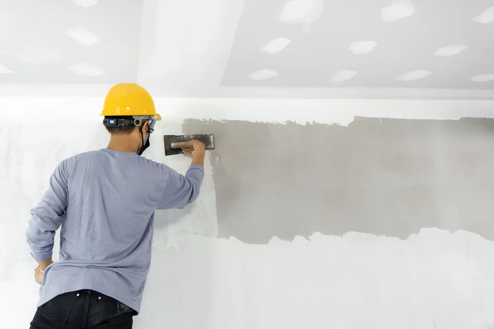 Un architecte ou ing&eacute;nieur en chemise &agrave; carreaux rouge travaille sur des plans techniques dans son bureau
