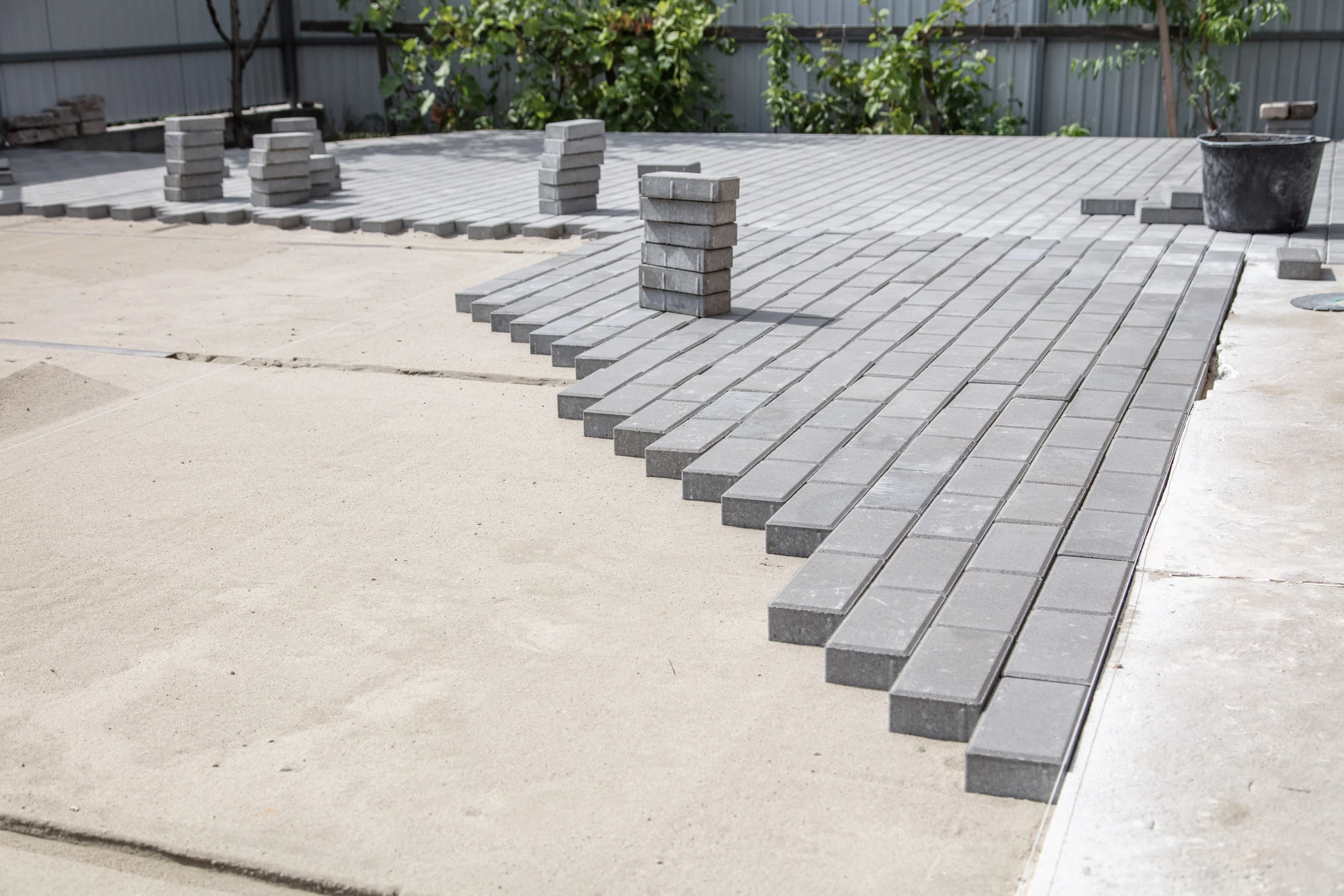 Dallage de jardin en construction, avec tuiles de patio en porcelaine grise et briques incurvées en bordure de fusain